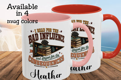 Two white ceramic mugs with pink and orange-red interiors and handles, shown on a wooden surface with a blurred beach background. The front mug has a printed graphic with books, a rose, and the text 'I READ FOR THE BAD INFLUENCE and stayed for the CONSEQUENCES' with 'Heather' below.