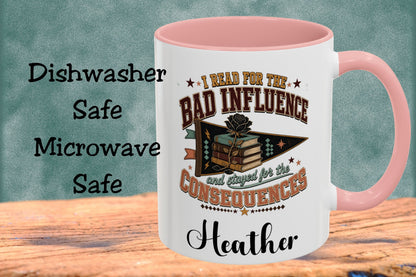 A white ceramic mug with a pink handle and interior, featuring a book-themed graphic and the text 'I Read For The Bad Influence and stayed for the Consequences' and the name 'Heather'. The mug sits on a wooden surface against a textured teal background, with text on the left reading 'Dishwasher Safe Microwave Safe'.
