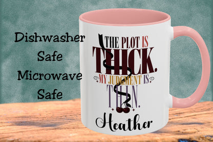 A white ceramic mug with a pink interior and handle, featuring the quote 'THE PLOT IS THICK. MY JUDGMENT IS THIN.