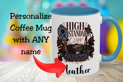 A white coffee mug with a blue handle and blue interior, printed with decorative text and illustration reading 'HIGH STANDARDS LOW FICTIONAL JUDGMENT' and 'Leather.' Large overlaid text says 'Personalize Coffee Mug with ANY name' with a red arrow pointing to the mug.