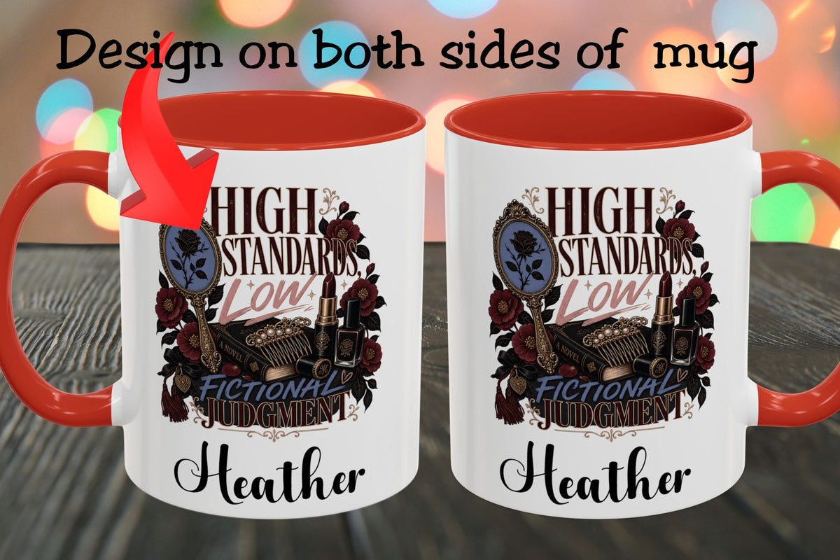 Two white ceramic mugs with orange-red interiors and handles are shown side by side on a dark wooden surface. The mugs feature a vintage-style graphic with the text 'HIGH STANDARDS LOW FICTIONAL JUDGEMENT' and the name 'Heather' printed below, plus a red arrow pointing to the left mug.