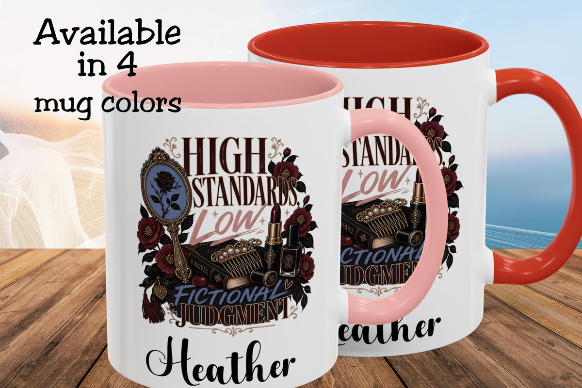 Two white ceramic mugs with pink and orange-red interiors and handles, shown on a wooden surface with a blurred beach background. The mugs feature a decorative graphic with the words 'HIGH STANDARDS LOW FICTIONAL JUDGMENT' and the name 'Heather'.