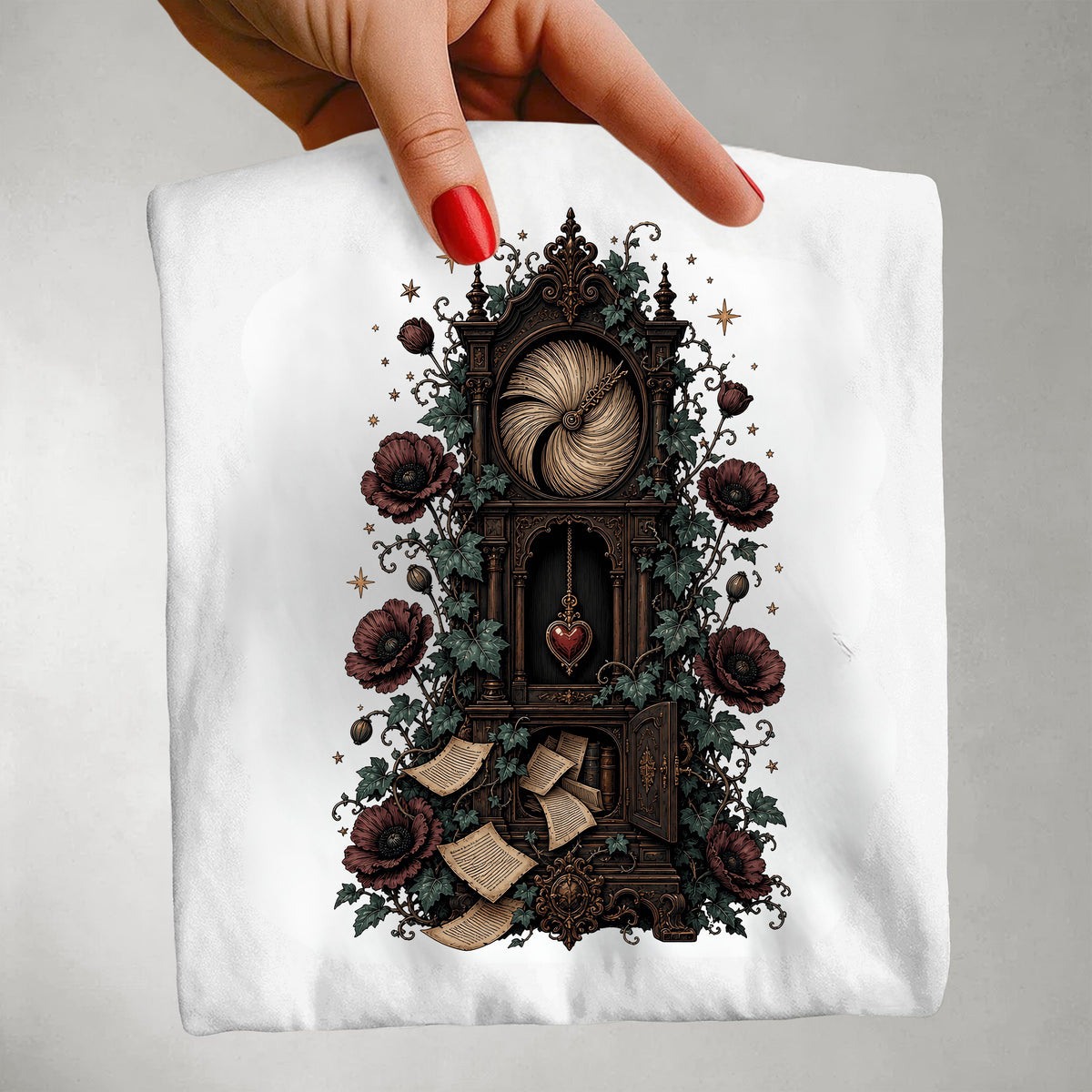 A hand with red nail polish holds up a white t-shirt featuring a detailed graphic print of a gothic clockwork mechanism adorned with dark red roses, green leaves, and gold stars.