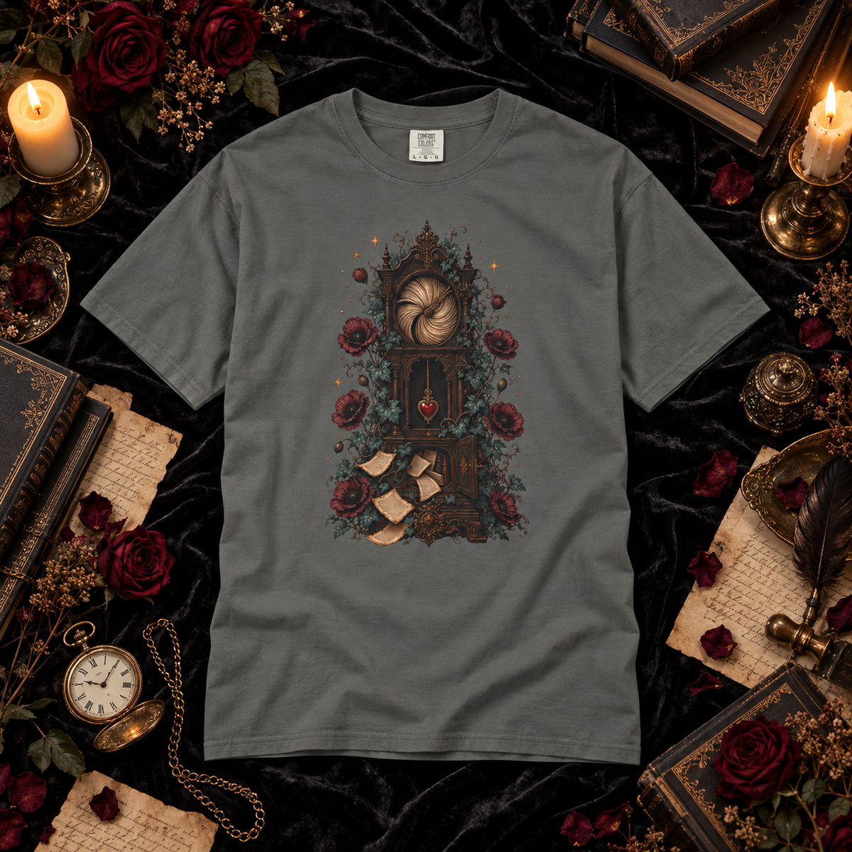 A dark gray crewneck t-shirt featuring a gothic-style graphic of a clockwork mechanism surrounded by red roses and gold coins, presented in a styled flat-lay with candles, books, and a pocket watch on a black velvet background.