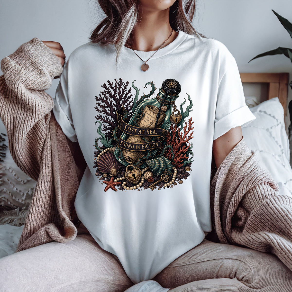 A woman wearing a white oversized graphic T-shirt with a detailed ocean-themed print featuring a bottle, shell, starfish, coral, and the text 'LOST AT SEA. SEARCH IN DEPTH.