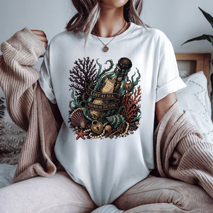 A woman wearing a white oversized graphic T-shirt with a detailed ocean-themed print featuring a bottle, shell, starfish, coral, and the text 'LOST AT SEA. SEARCH IN DEPTH.