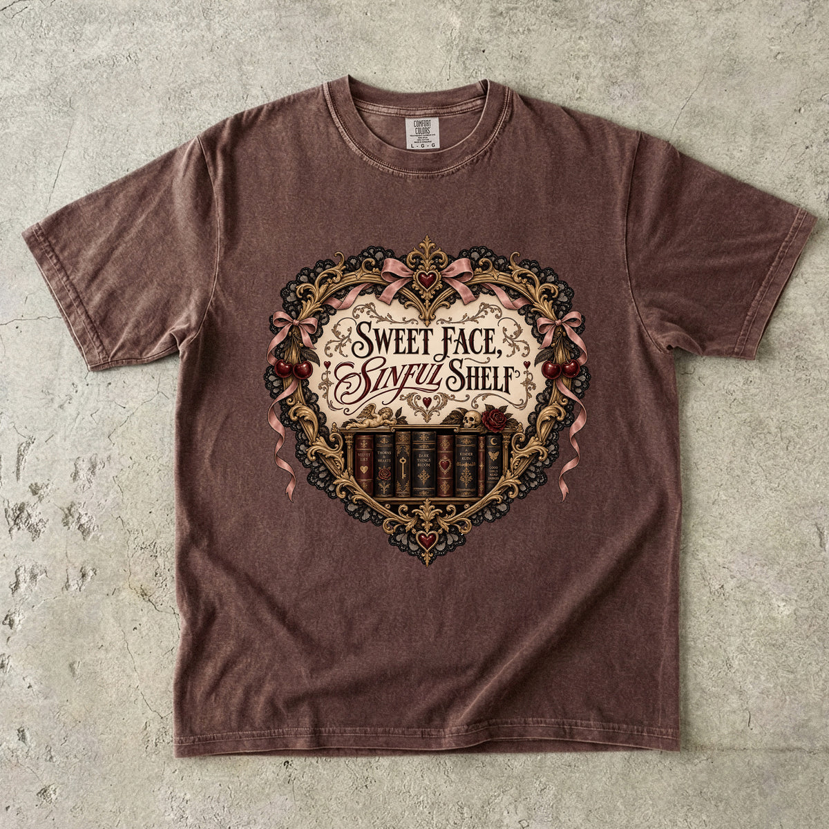 A brown short-sleeve t-shirt with a vintage-style gothic graphic on the chest reading 'Sweet Face, Simple Shelf' with ornate gold and pink details, laid flat on a textured gray concrete surface.