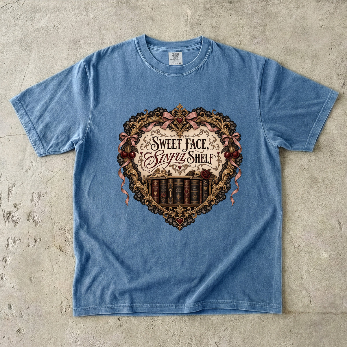 A light blue short-sleeve t-shirt laid flat on a textured concrete surface, featuring a large vintage-style graphic on the chest with a heart-shaped bookshelf design and the text 'Sweet Face and Sorry Shelf'.