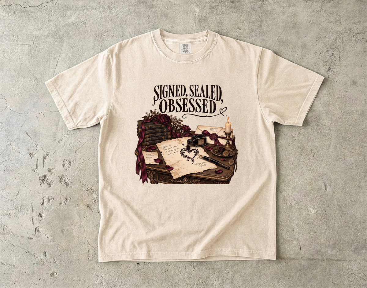 An off-white crewneck t-shirt with a gothic graphic print reading 'SIGNED, SEALED, OBSESSED' above an illustration of a desk with a quill, candle, and letter, laid flat on a textured gray concrete background.