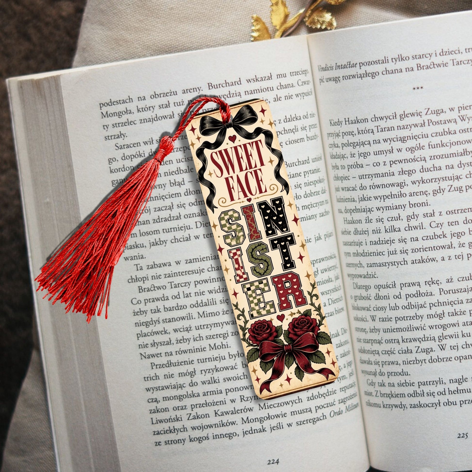 A decorative wooden book bookmark with a red tassel and red roses, reading 'READ MORE IN THE BIBLE' in Polish, placed on an open book.