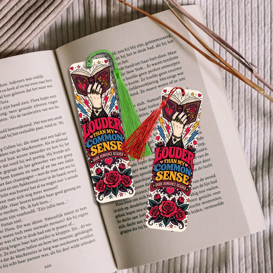 Two decorative bookmarks with a colorful tattoo-style illustration of a woman and roses, placed on an open book with two wooden sticks on a light wood surface.