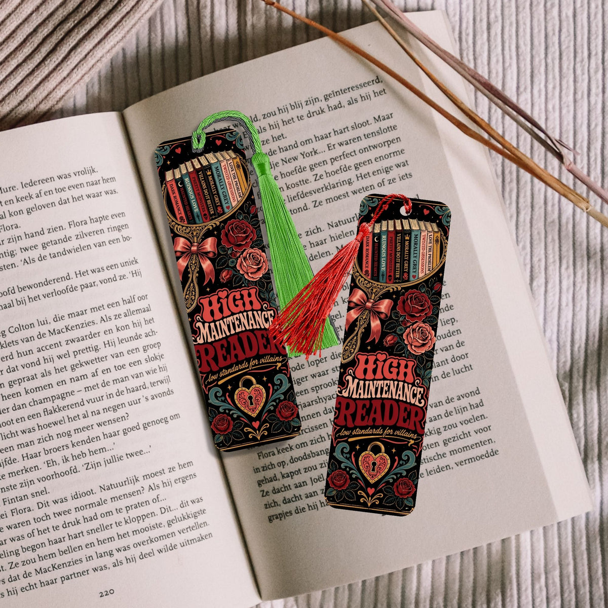 Two decorative book-shaped bookmarks with tassels resting on open book pages, with wooden sticks in the background.