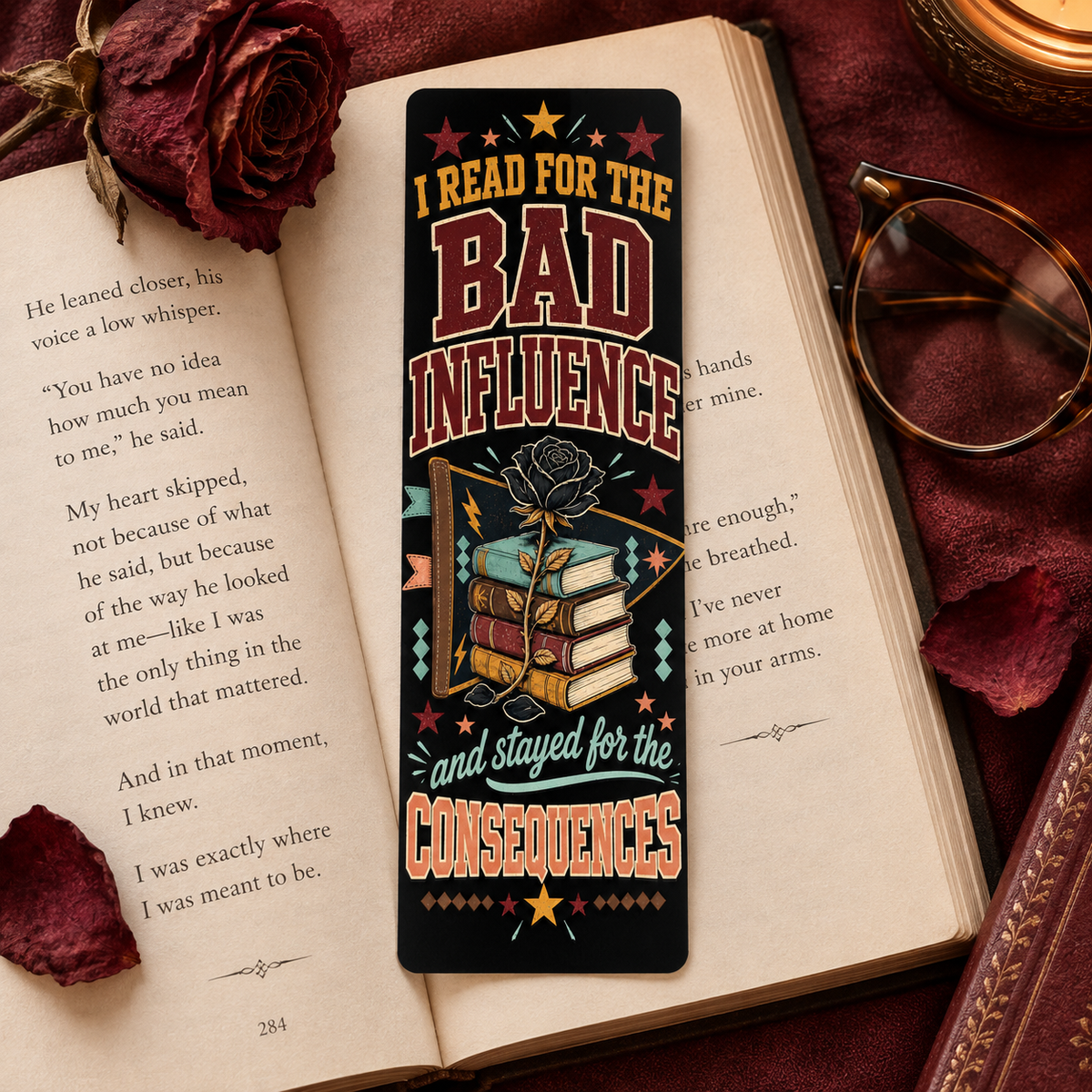 A rectangular book bookmark with a dark background and a colorful graphic of stacked books tied with a rose, placed on an open book. The bookmark features the text 'I READ FOR THE BAD INFLUENCE and stayed for the CONSEQUENCES' with stars and decorative accents.