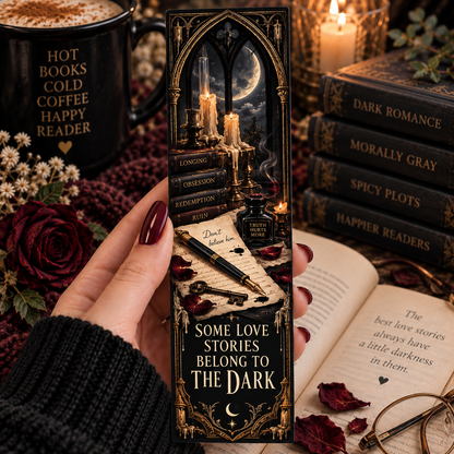 A hand holds a tall black gothic-themed book bookmark with ornate gold illustration of a moonlit scene and the text 'SOME LOVE STORIES BELONG TO THE DARK.' The scene is styled with books, a mug reading 'HOT BOOKS COLD COFFEE HAPPY READER,' candles, roses, and an open book.